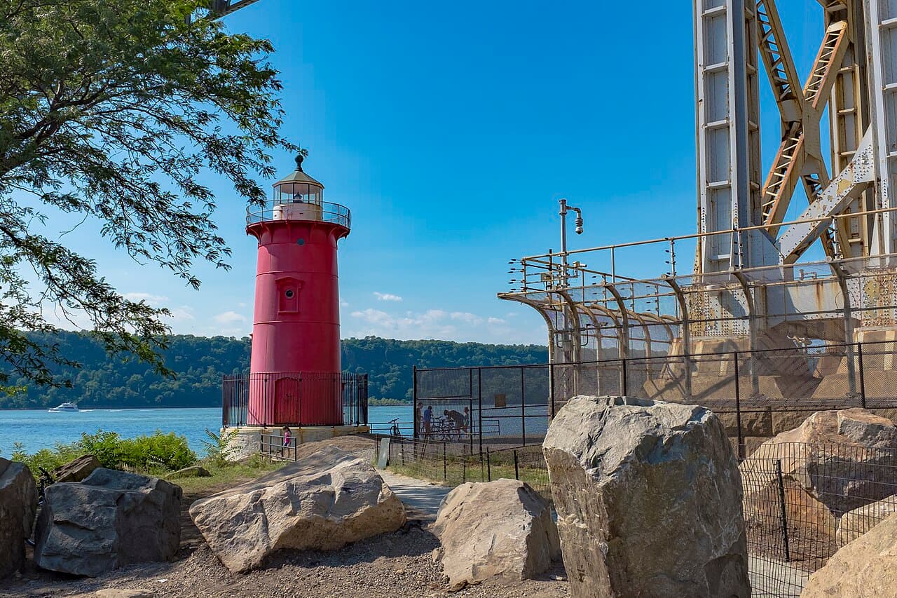 The Little Red Lighthouse on the Hudson River shoreline, beside a steel tower of the George Washington Bridge